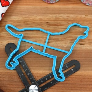 Peut inclure: Un emporte-pi&egrave;ce en plastique bleu en forme de chien sur une surface en bois. L'emporte-pi&egrave;ce a un contour d&eacute;taill&eacute; d'un chien avec un bord sur&eacute;lev&eacute;.