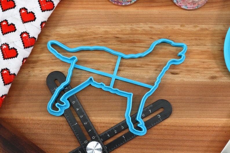 Peut inclure: Un emporte-pi&egrave;ce en plastique bleu en forme de chien sur une surface en bois. L'emporte-pi&egrave;ce a un contour d&eacute;taill&eacute; d'un chien avec un bord sur&eacute;lev&eacute;.