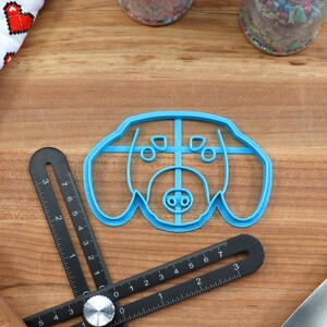 May include: A blue plastic cookie cutter shaped like a dog's head. The cutter has a detailed design with a nose, eyes, and ears.