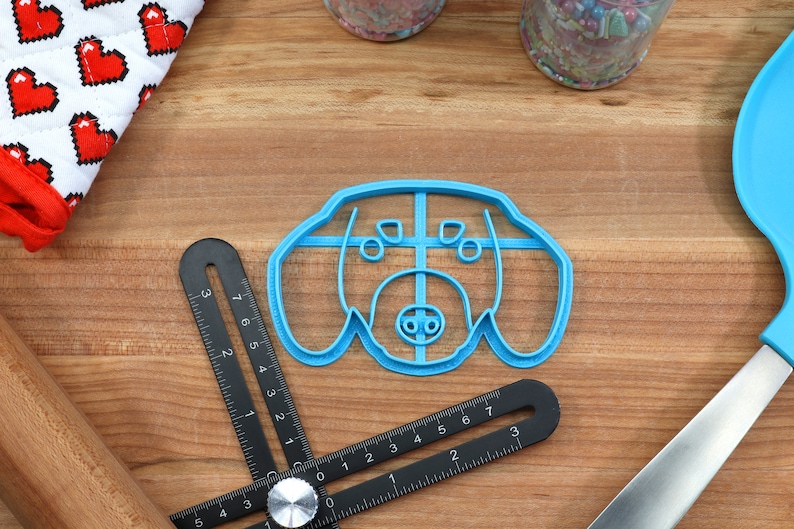May include: A blue plastic cookie cutter shaped like a dog's head. The cutter has a detailed design with a nose, eyes, and ears.