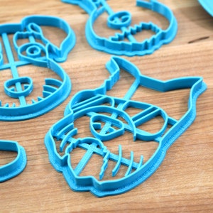 May include: Four blue plastic cookie cutters shaped like dogs. The cutters have detailed features, including ears, eyes, noses, and mouths.
