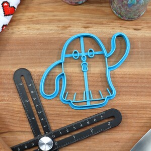 May include: A blue plastic ghost-shaped cookie cutter with a friendly face and outstretched arm.
