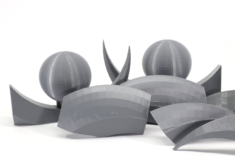 May include: A set of gray 3D printed geometric shapes, including spheres and curved pieces. The shapes are arranged in a cluster on a white background.