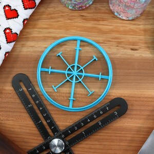 May include: A blue plastic circle cookie cutter with a starburst design. The cutter is on a wooden surface with a ruler and a spatula.