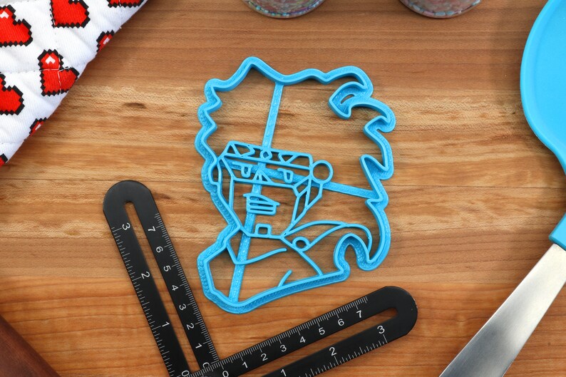 May include: Blue plastic cookie cutter shaped like a cartoon character with spiky hair. The character has a large head and a small body.