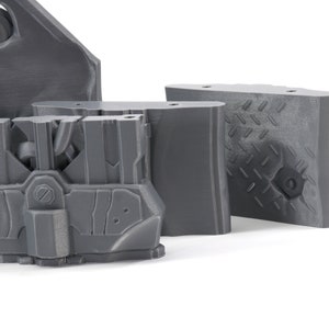 May include: A set of four gray 3D printed plastic pieces with intricate designs. The pieces are made of a smooth, matte plastic and have a variety of shapes and textures.