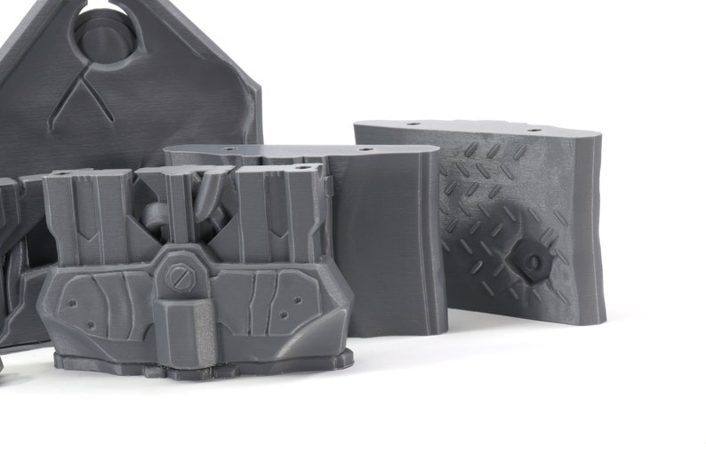 May include: A set of four gray 3D printed plastic pieces with intricate designs. The pieces are made of a smooth, matte plastic and have a variety of shapes and textures.