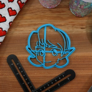 May include: A blue plastic cookie cutter shaped like a cartoon character with short hair and pointy ears.