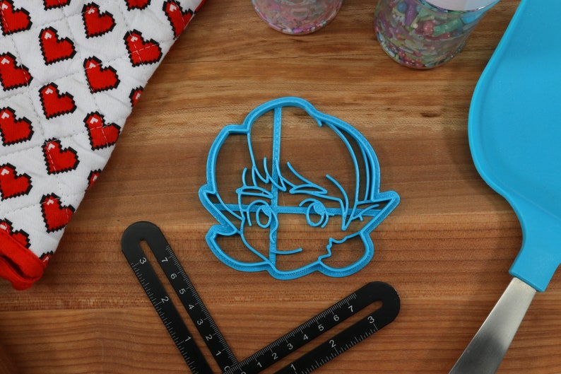 May include: A blue plastic cookie cutter shaped like a cartoon character with short hair and pointy ears.