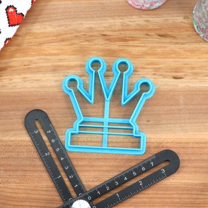 May include: A blue plastic crown-shaped cookie cutter on a wooden surface.
