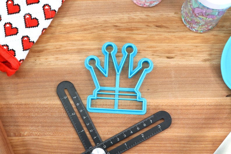 May include: A blue plastic crown-shaped cookie cutter on a wooden surface.