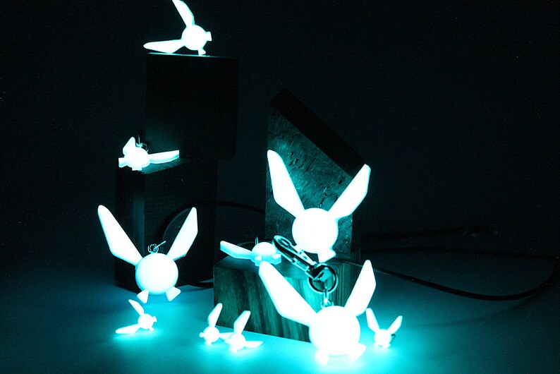 May include: A collection of glowing blue fairy keychains with wings, some are on a wooden surface and others are on a black surface.