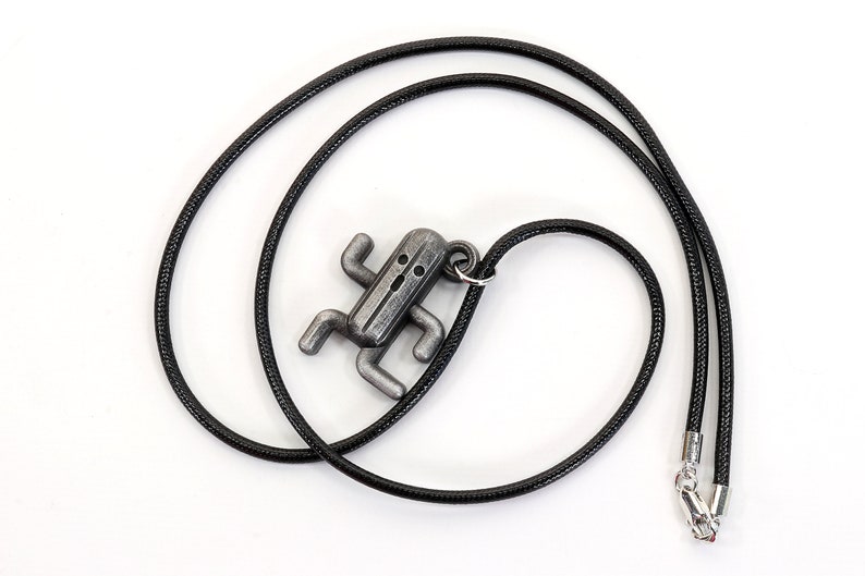 May include: A silver-colored pendant necklace featuring a stylized character from a popular video game. The pendant is attached to a black cord.