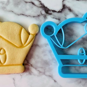 May include: A blue plastic cookie cutter and a yellow sugar cookie, both shaped like a crown.