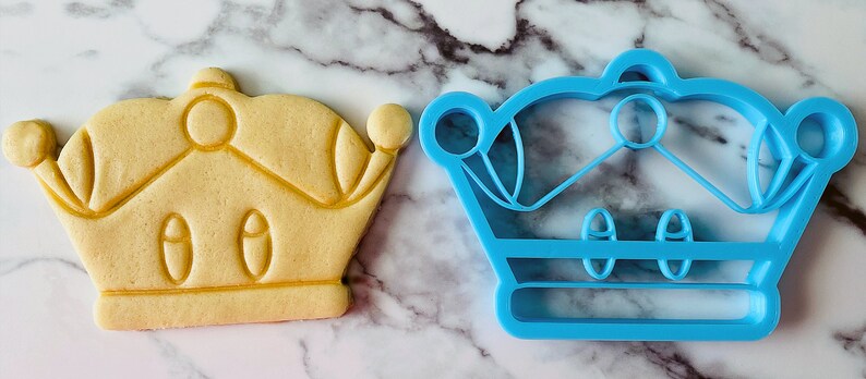 May include: A blue plastic cookie cutter and a yellow sugar cookie, both shaped like a crown.