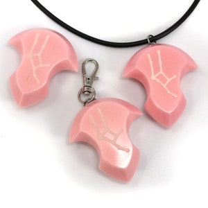 May include: Three pink resin pendants with a white Gemini zodiac symbol. The pendants are attached to a black cord necklace and a silver key chain.