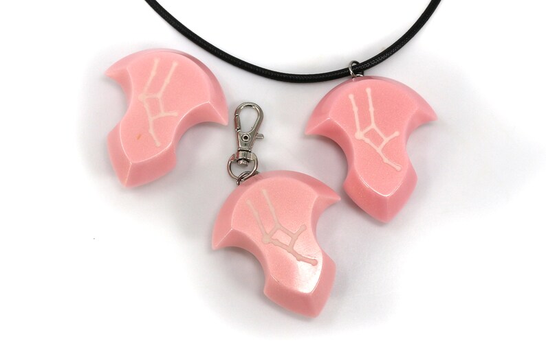 May include: Three pink resin pendants with a white Gemini zodiac symbol. The pendants are attached to a black cord necklace and a silver key chain.