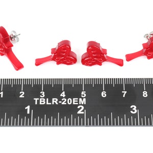 May include: Four red plastic earrings shaped like a heart with a swirl design. The earrings are about 1 inch long and are shown next to a ruler.