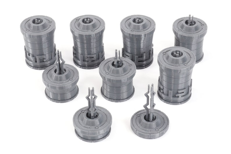 May include: Eight gray 3D printed miniature towers with intricate designs. The towers are cylindrical with a circular base and a pointed top. The towers are arranged in a random pattern on a white surface.