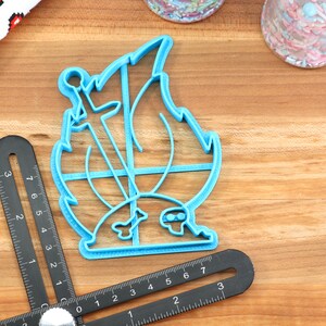 May include: A blue plastic cookie cutter shaped like a cartoon character holding a sword. The character is wearing a blue bandana and has a sword in its right hand.