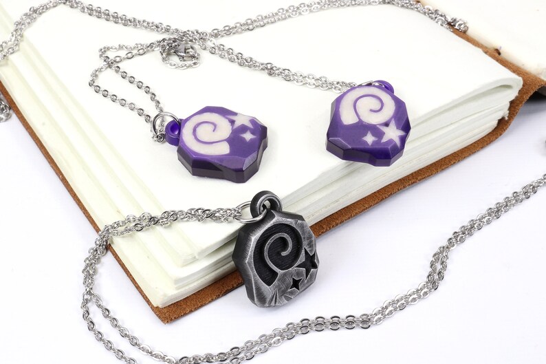May include: Two silver necklaces with purple and silver pendants featuring a spiral design and white stars.