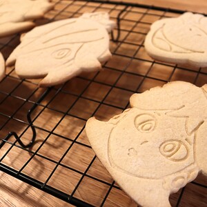 May include: Four sugar cookies decorated with icing and designs of cartoon characters on a black wire cooling rack.