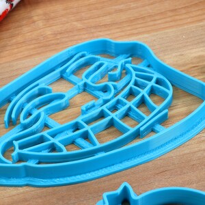 Puede incluir: Un cortador de galletas de pl&aacute;stico azul con forma de cara de meme con una amplia sonrisa y cejas levantadas.