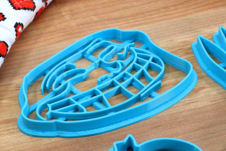 Puede incluir: Un cortador de galletas de pl&aacute;stico azul con forma de cara de meme con una amplia sonrisa y cejas levantadas.