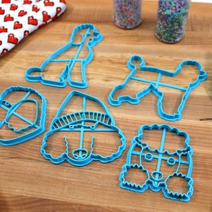 May include: Set of five blue plastic poodle cookie cutters. The cutters are in various shapes and sizes, including a full body poodle, a poodle head, and a poodle head wearing a hat.