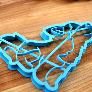 May include: A blue plastic cookie cutter shaped like a cartoon firefighter holding a hose. The cutter is on a wooden surface.