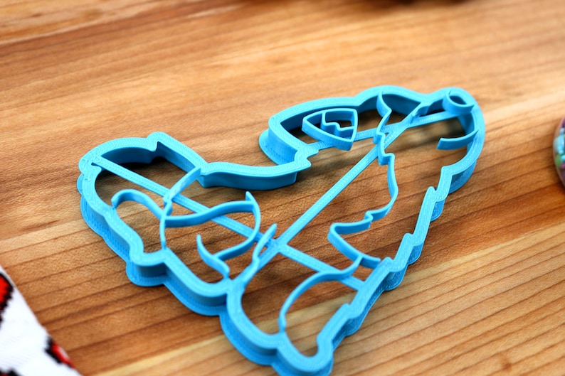 May include: A blue plastic cookie cutter shaped like a cartoon firefighter holding a hose. The cutter is on a wooden surface.