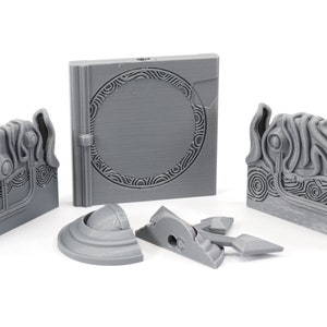 May include: A set of five gray 3D printed pieces, including a book-shaped piece with a circular design, two rectangular pieces with intricate designs, and two smaller pieces with rounded edges.