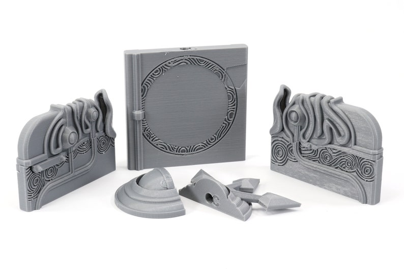 May include: A set of five gray 3D printed pieces, including a book-shaped piece with a circular design, two rectangular pieces with intricate designs, and two smaller pieces with rounded edges.