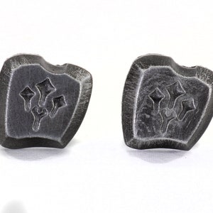 以下が含まれることがあります： 盾の形をした銀色の金属製のカフスボタンのペア。各カフスボタンには、スタイリッシュな花柄のモチーフが施されています。