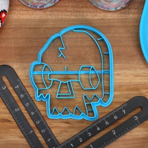 May include: Blue plastic cookie cutter shaped like a cartoon monster with a single eye and a jagged mouth.