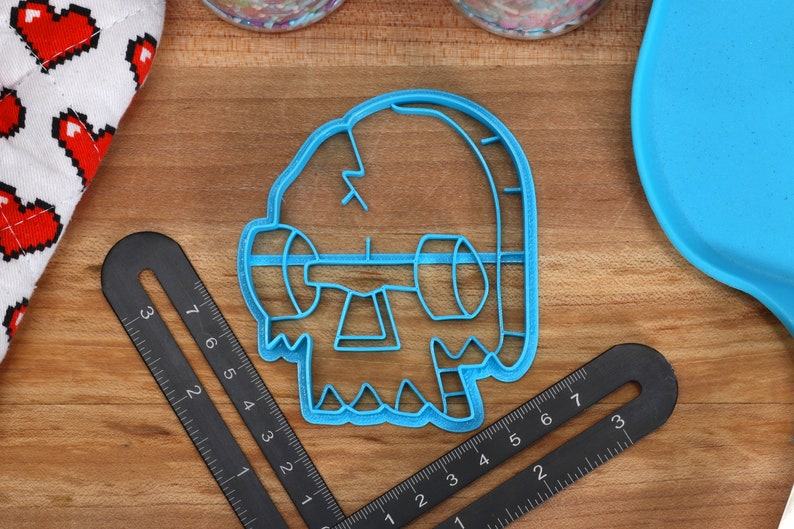 May include: Blue plastic cookie cutter shaped like a cartoon monster with a single eye and a jagged mouth.