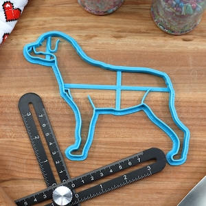 May include: A blue plastic dog-shaped cookie cutter on a wooden surface with a ruler and a spatula.