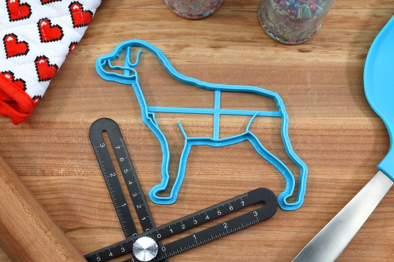 May include: A blue plastic dog-shaped cookie cutter on a wooden surface with a ruler and a spatula.