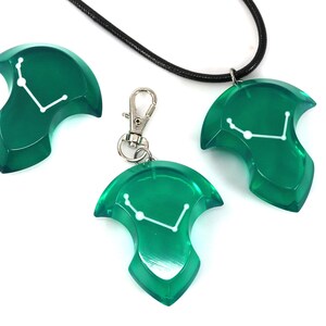 May include: A set of three green resin accessories: a pendant on a black cord, a keychain, and a separate charm. Each piece features a white constellation design. The items are displayed on a white background.