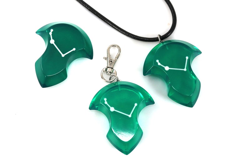 May include: A set of three green resin accessories: a pendant on a black cord, a keychain, and a separate charm. Each piece features a white constellation design. The items are displayed on a white background.