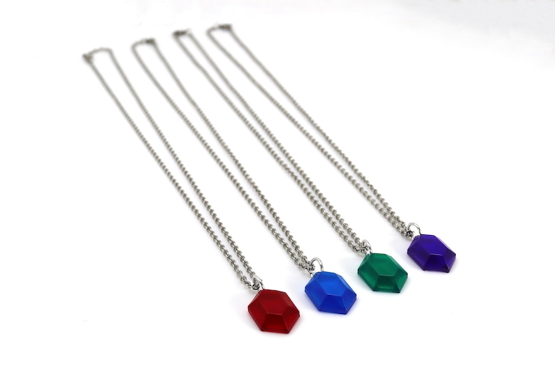 May include: Four silver necklaces with different colored gem pendants. The pendants are red, blue, green, and purple.
