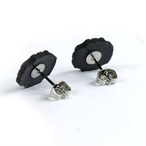 May include: A pair of black stud earrings with silver posts and backs. The earrings are shaped like a flower with a rough, textured surface.