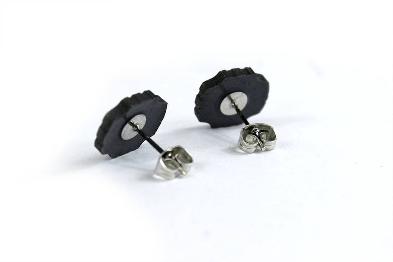 May include: A pair of black stud earrings with silver posts and backs. The earrings are shaped like a flower with a rough, textured surface.