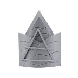 May include: A gray 3D printed crown with a triangle design and wavy lines. The crown is made of plastic and has a smooth finish.