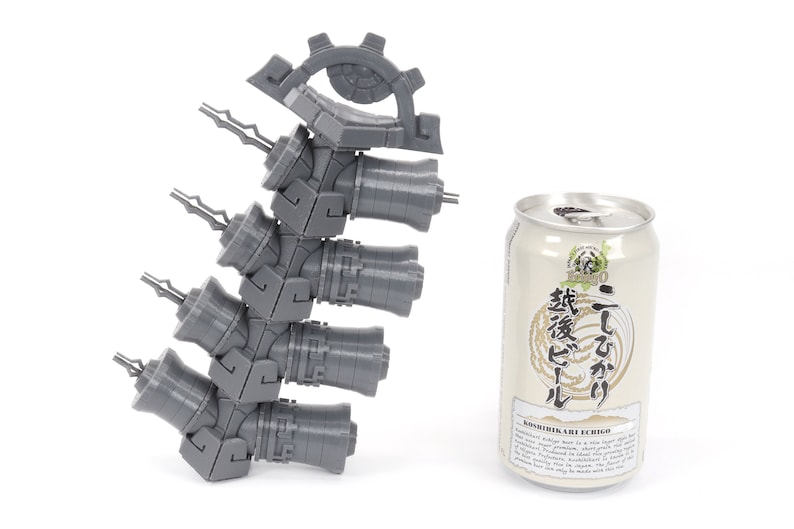 May include: A gray 3D printed model of a mechanical device with a gear and multiple cylinders. The model is about the size of a can of beer.