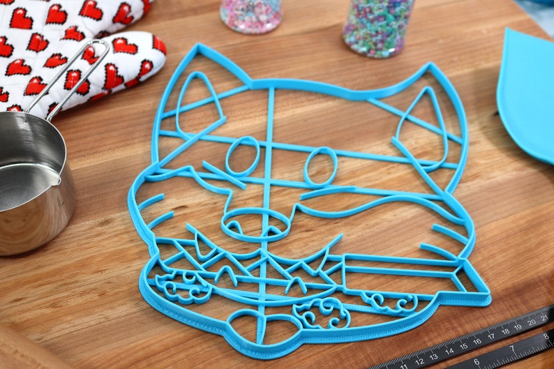 May include: A blue plastic cookie cutter shaped like a cartoon fox with a detailed face and a grid pattern on the body.