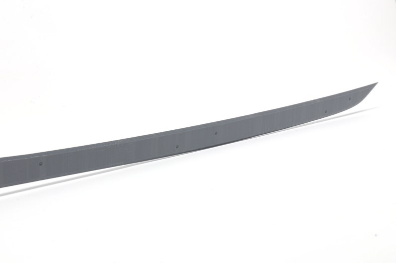 May include: A gray metal sword with a slightly curved blade. The blade has a textured surface and a dull finish.