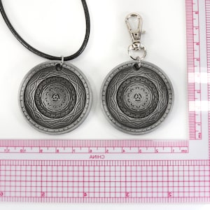 May include: Two silver-toned pendants with a geometric design. One pendant is on a black cord necklace, the other is on a silver chain with a lobster clasp. Both pendants feature a circular design with a triangle in the center.
