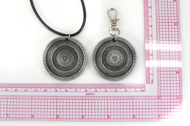 May include: Two silver-toned pendants with a geometric design. One pendant is on a black cord necklace, the other is on a silver chain with a lobster clasp. Both pendants feature a circular design with a triangle in the center.