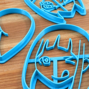 May include: Three blue plastic cookie cutters, one shaped like a heart, one shaped like a face, and one shaped like a flower.